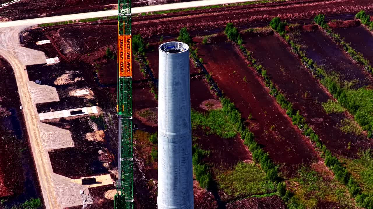 Torre eolica in fase di assemblaggio con una gru in un cantiere di parco eolico. Ripresa aerea con inclinazione verso il basso e movimento in avanti.