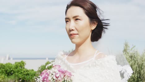 Video-of-happy-asian-bride-walking-holding-bouquet-and-smiling-at-outdoor-wedding