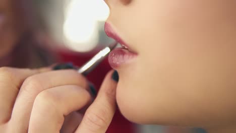 Close-Up-view-of-a-professional-makeup-artist's-hand-using-special-brush-to-apply-lipstick-on-model's-lips-working-in-beauty