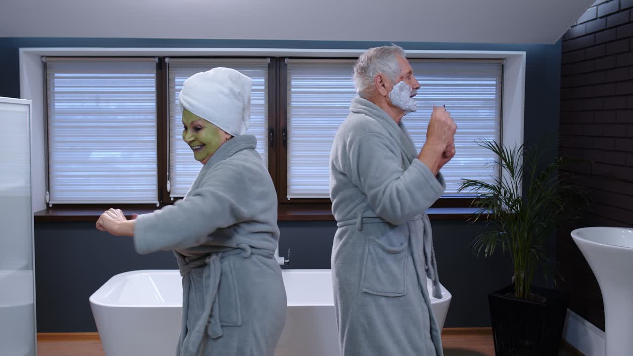 Elderly grandmother with facial green mask and grandfather with shaving foam dancing in bathroom