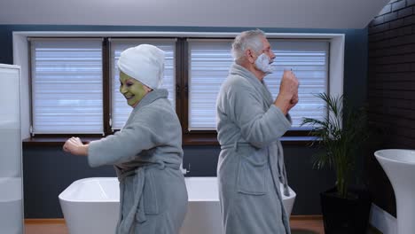 elderly grandmother with facial green mask and grandfather with shaving foam dancing in bathroom