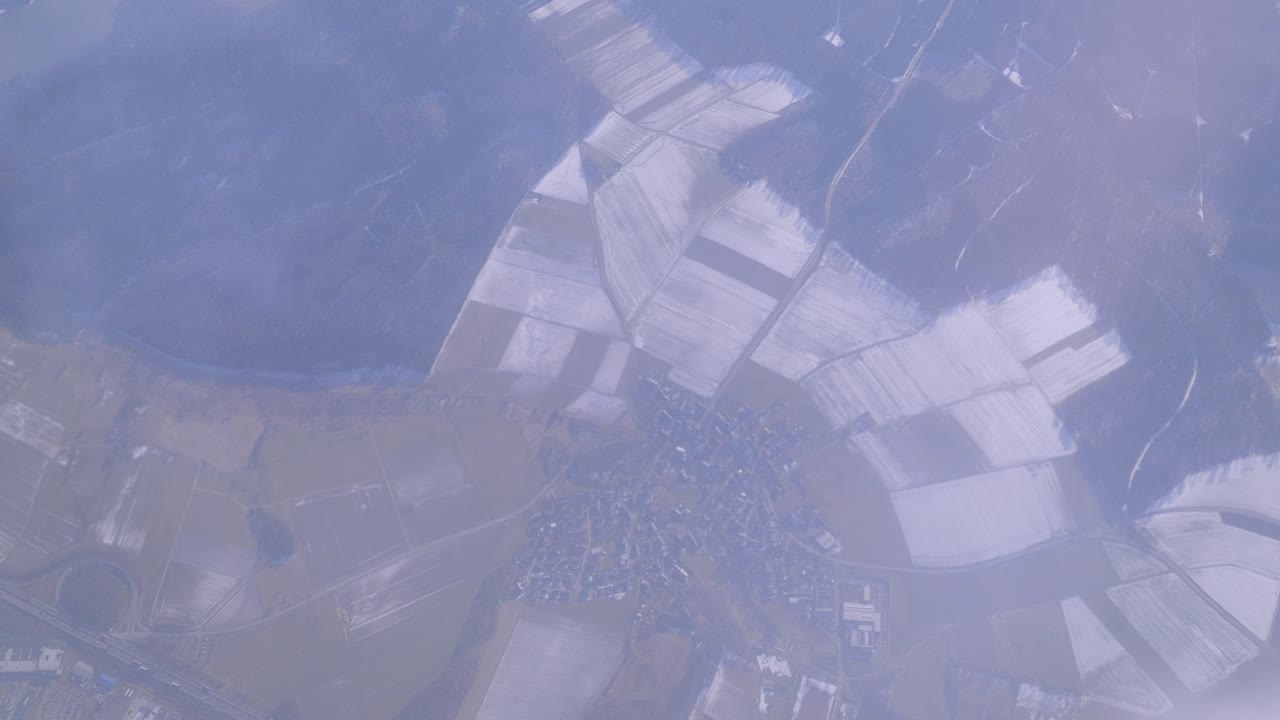 Snowy fields with roads and a small village below on a cloudy day, aerial view