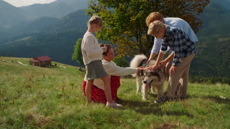 family spending holiday dog in mountains. parents with children petting husky.