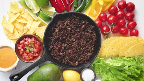 ingredientes para chili con carne en una sartén de hierro sobre una mesa de madera blanca