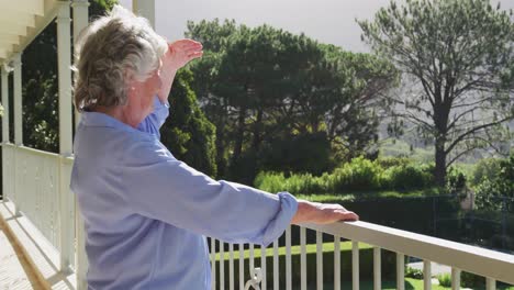 mujer mayor caucásica sonriente en casa disfrutando de la vista del jardín soleado desde el balcón