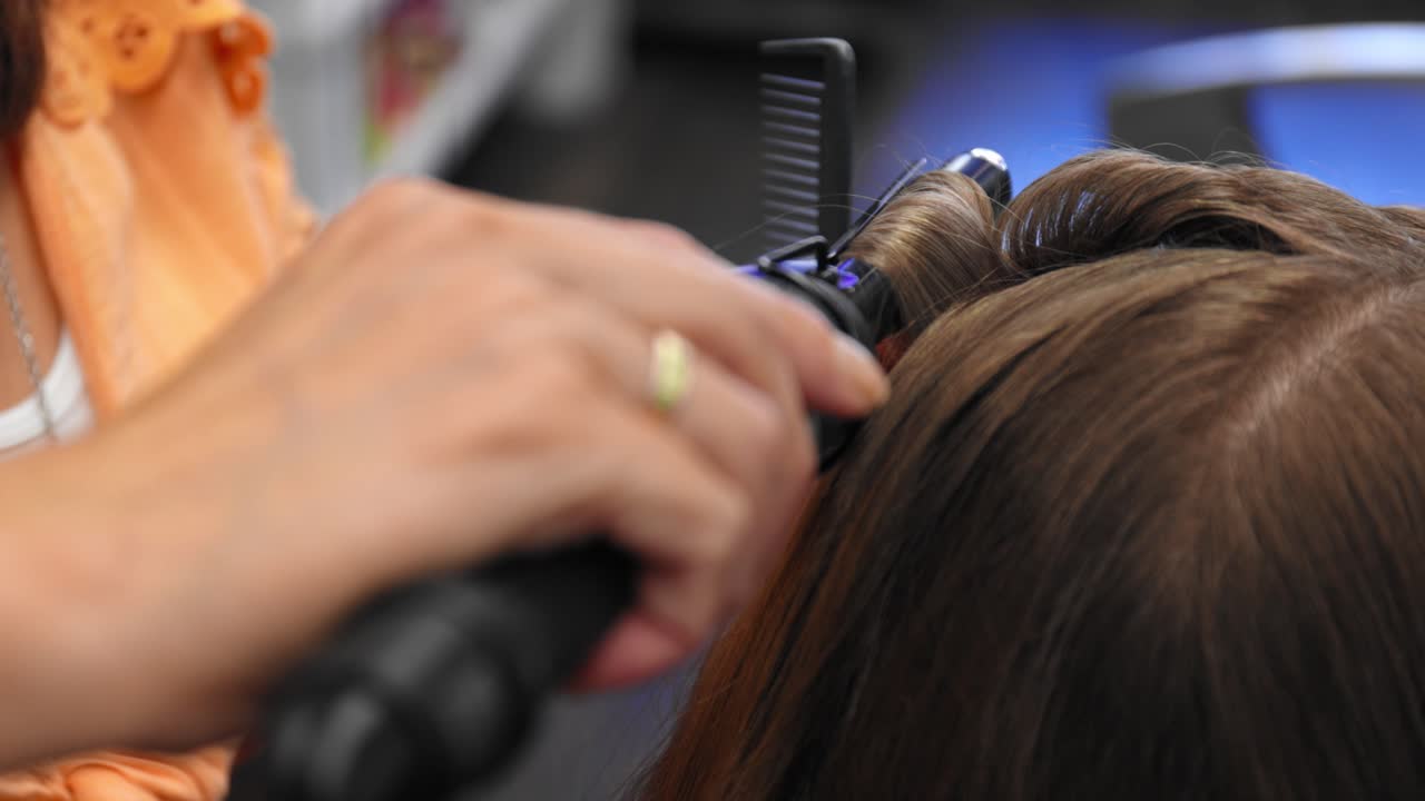 컬링 지팡이에 갈색 머리를 빙빙 돌린 다음 잡고있는 여성