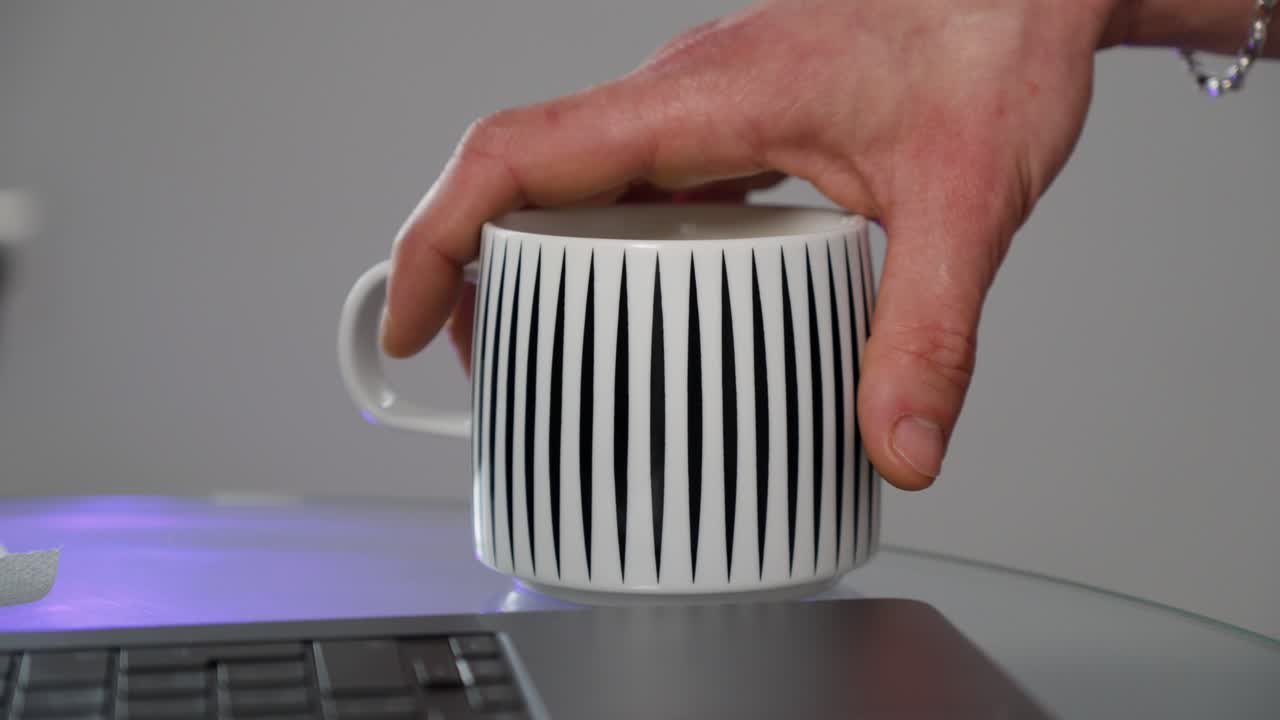 hand holding a coffee mug at the side of a laptop whilst working from home