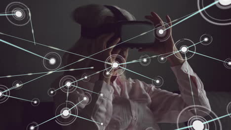 Animation-of-communication-network-over-senior-caucasian-woman-using-vr-headset-in-dark-room