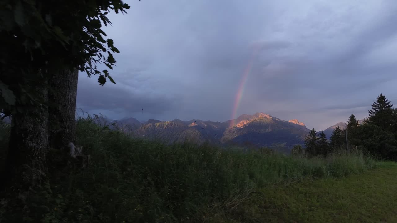 Drone fly out of Forest reveal Mountain Range with Rainbow in Background Early Morning