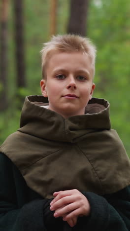 blond boy in vintage costume leans on sword in spring forest slow motion. young actor at historical film set. child of medieval period at quest