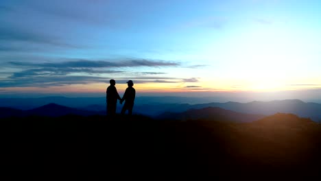 the couple on standing on the evening mountain on the bright sun background