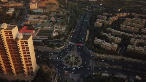 high angle aerial shot over towers in sunset near the square in big city tehran iran cars drive in streets taxi stop at taxi station and cityscape and green spaces in background landscape