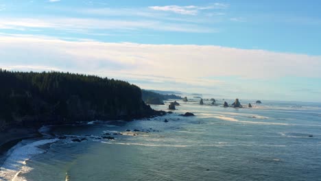 stunning aerial drone trucking right shot of the gorgeous third beach in forks, washington with large rock formations, cliffs, small waves and sea foam on a warm sunny summer morning