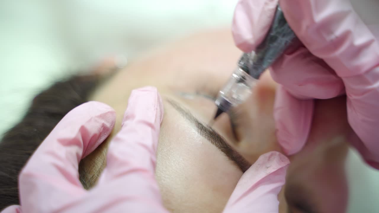 beautician is drawing the shape of eyebrows with needle for a woman in a beauty salon. Professional equipment for permanent makeup. Modern cosmetology. Blurred background