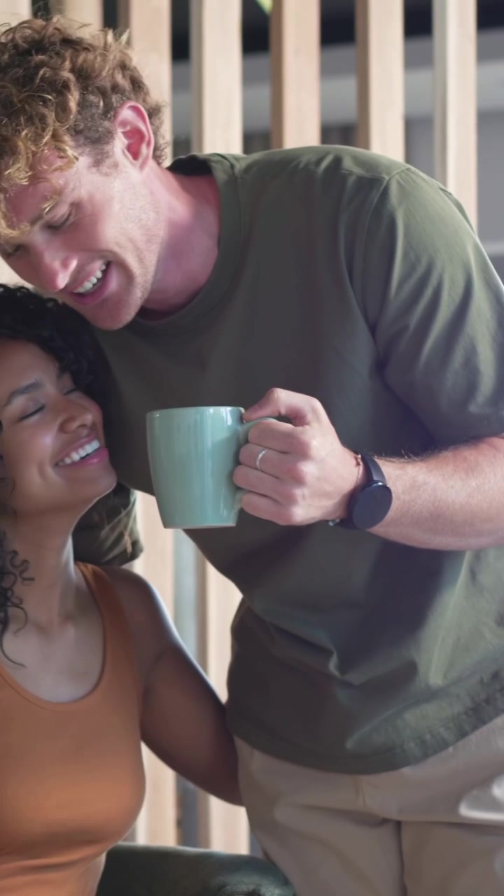 Video vertical: Hombre entrando con taza aguamarina, inclinándose hacia su pareja en la cocina, ofreciendo una cuchara.