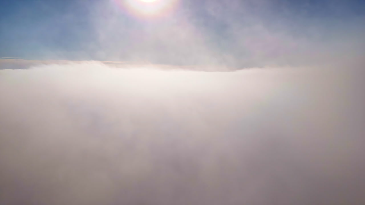 Aerial view above fluffy clouds with sun shining in blue sky