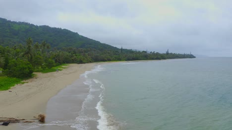 Aerial-footage-gliding-to-the-left-showing-a-palm-fringed-beach,-drenched-in-rainfall-and-shrouded-in-a-misty-haze