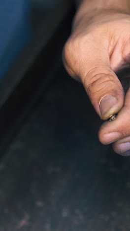 cu: professional jeweler connects rings of gold chain at dark wooden table with pliers in workshop extreme closeup