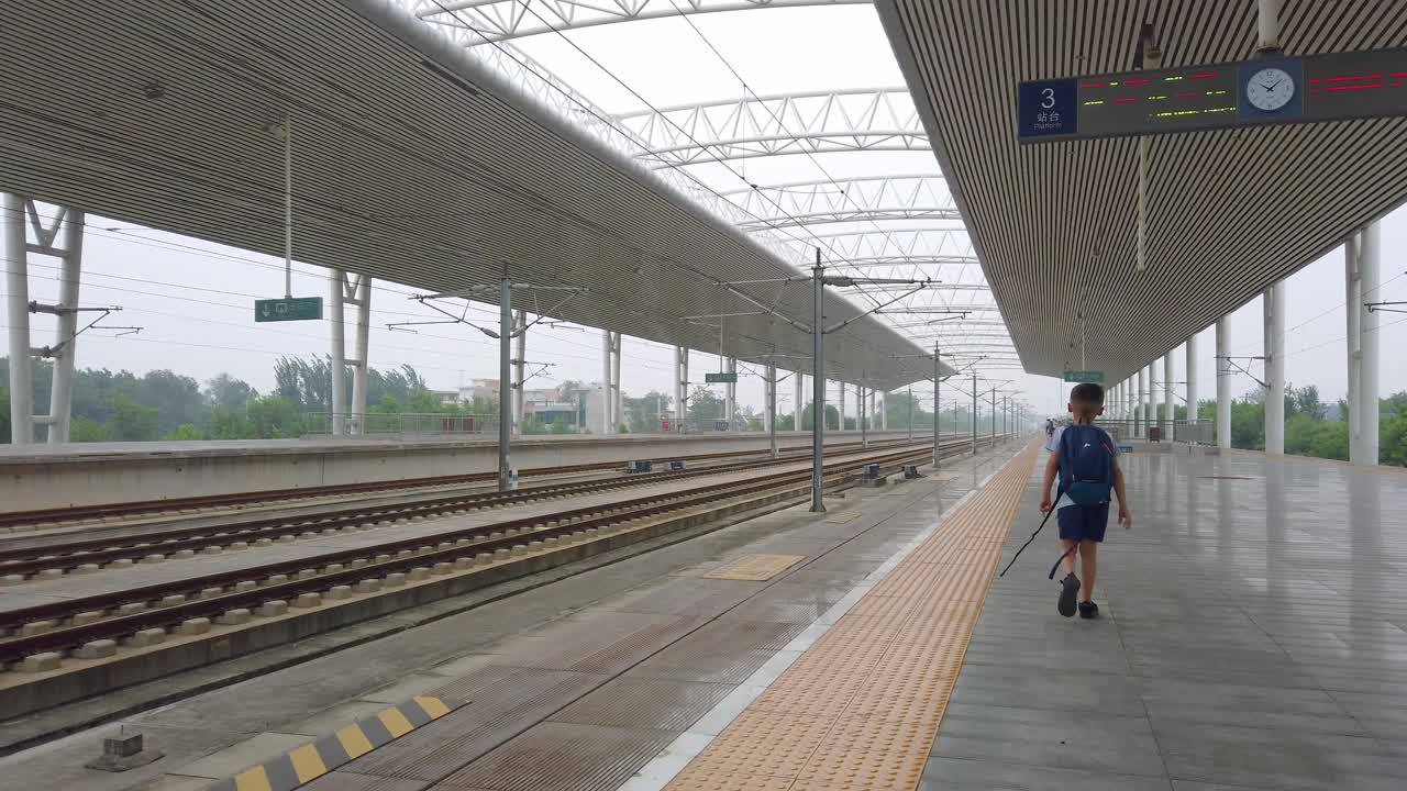 Little Caucasian boy with a small backpack walking on an empty platform while waiting for the arrival of the super fast Chinese high speed bullet train