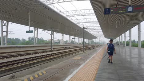 little caucasian boy with a small backpack walking on an empty platform while waiting for the arrival of the super fast chinese high speed bullet train