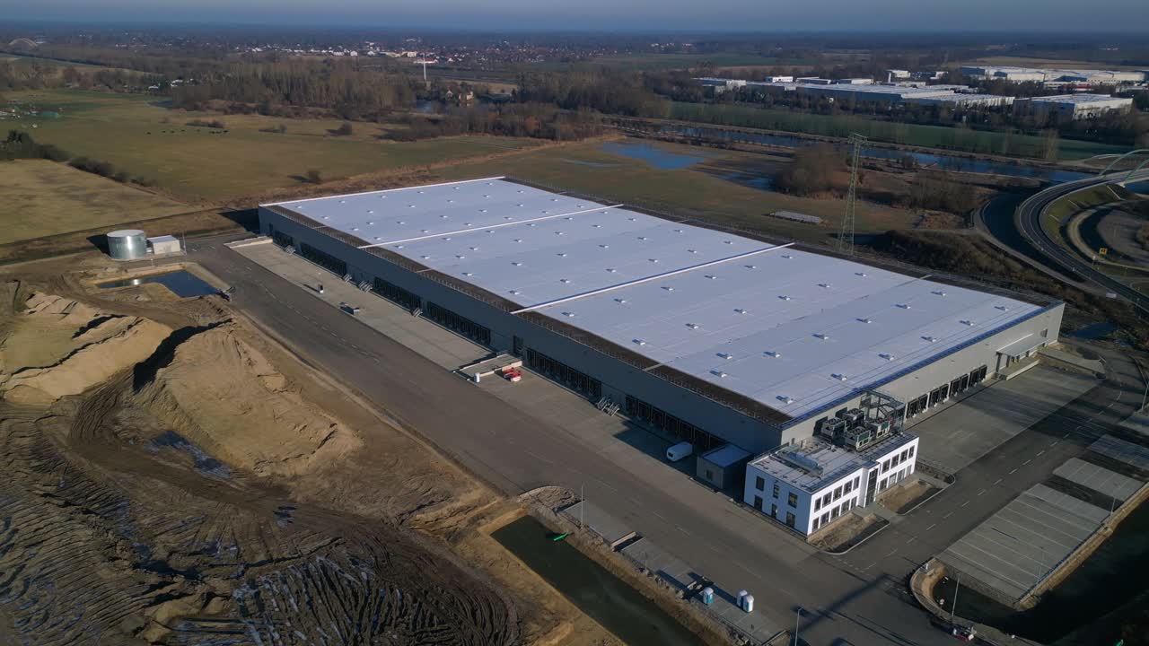 Nuovo grande centro logistico in costruzione con un'ampia area di stoccaggio, banchine di carico e terreno vuoto circostante. Splendida vista aerea ascendente ripresa con drone.
