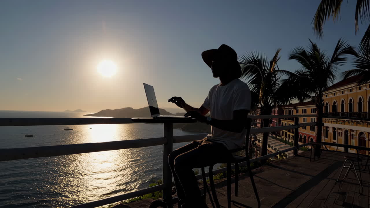 Man working on laptop at sunset overlooking ocean