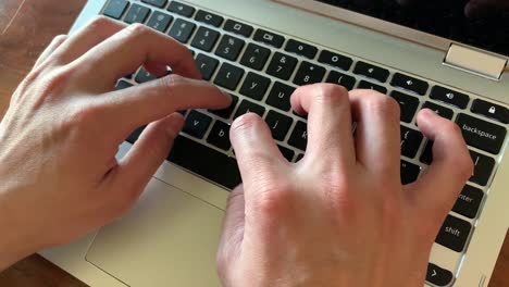 manos escribiendo en una computadora portátil con luz natural proveniente de la ventana de la oficina