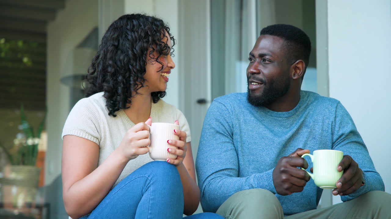 Smiling couple enjoying coffee together on porch, sharing warm conversation