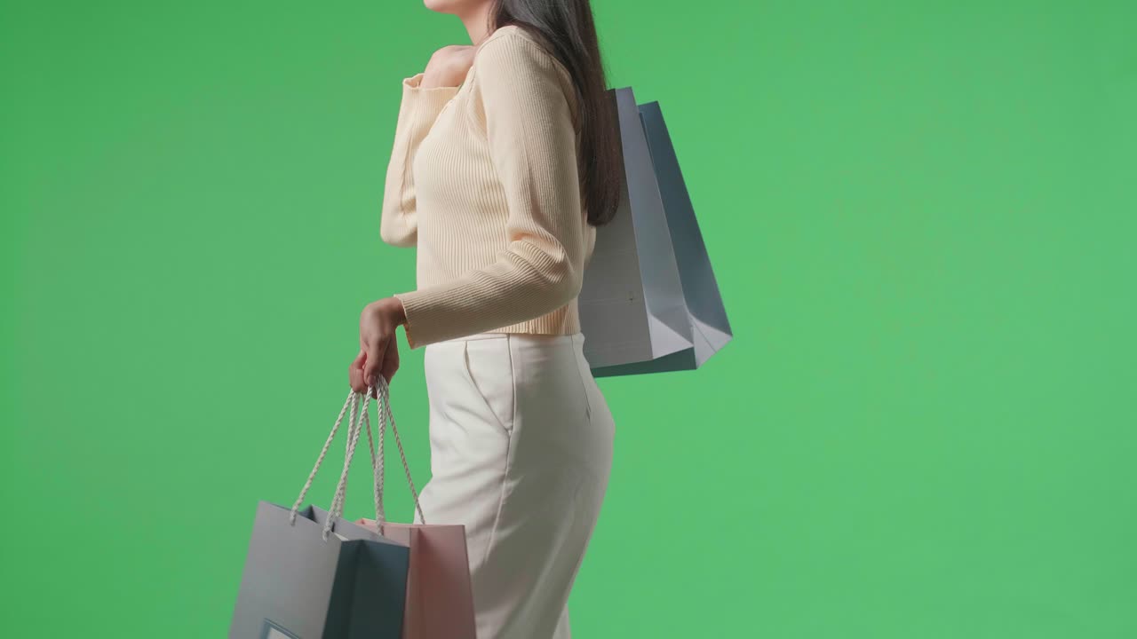 Side View Of A Shopping Woman With Shopping Bags Walking In Front Of Green Screen