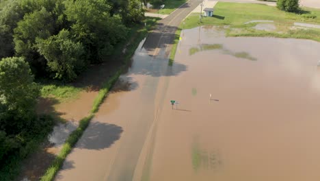 4k rising aerial view showing flood water going over a road outside of a small town