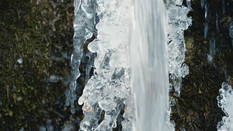 small waterfall in front of an icicle in a frozen river in winter, close up, real-time