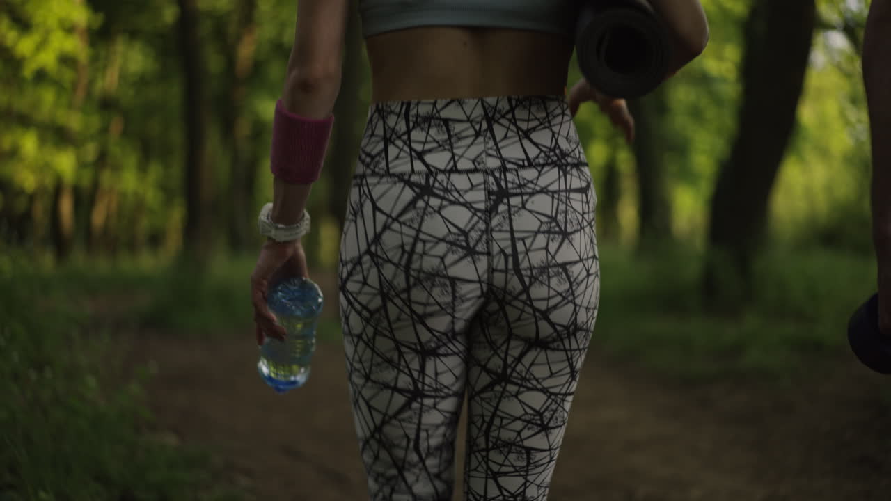 Woman walking in the forest with yoga mat and water bottle