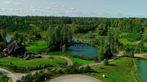 aerial drone forward moving shot over wooden houses beside small lakes surrounded by lush green vegetation at daytime