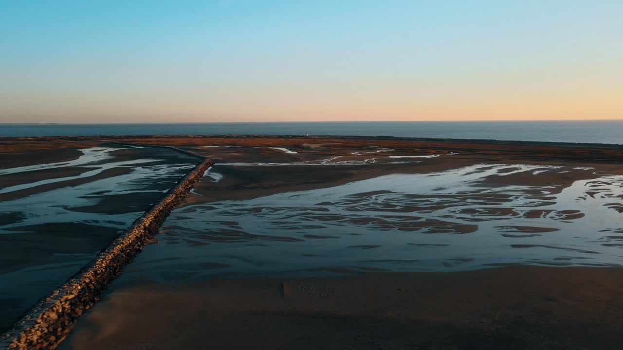 vuelo aéreo hacia adelante sobre el campo de marea baja con rompeolas y océano en el fondo a la hora de la puesta del sol