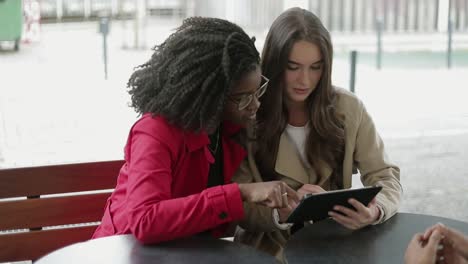 afro-american and caucasian women swiping photos on tablet