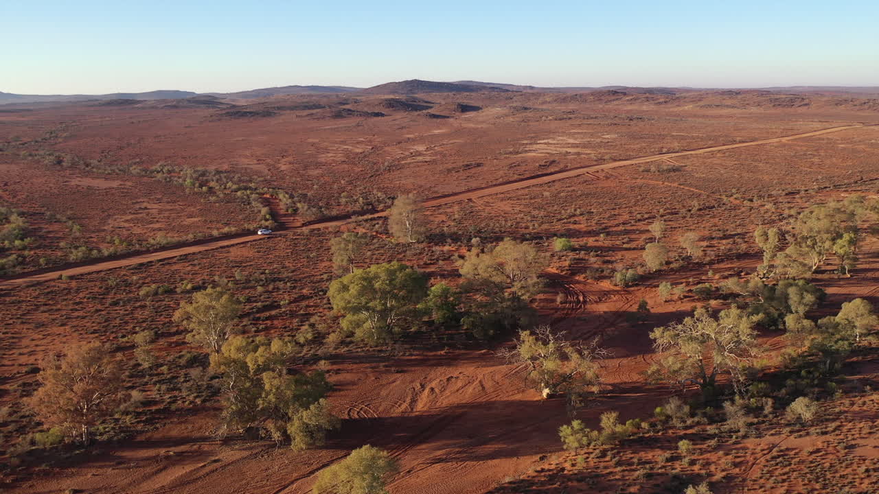 Aerea: Ripresa con drone che segue un veicolo bianco mentre guida lungo una strada sterrata polverosa nell'outback in lontananza, mentre si allontana, a Broken Hill, Australia