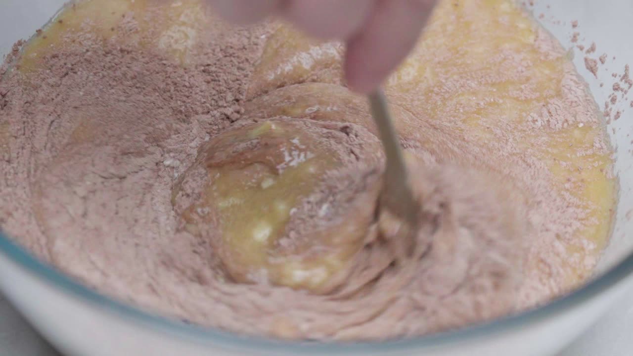Close-up of flour added to mashed bananas and mixed with a wooden spoon for banana bread