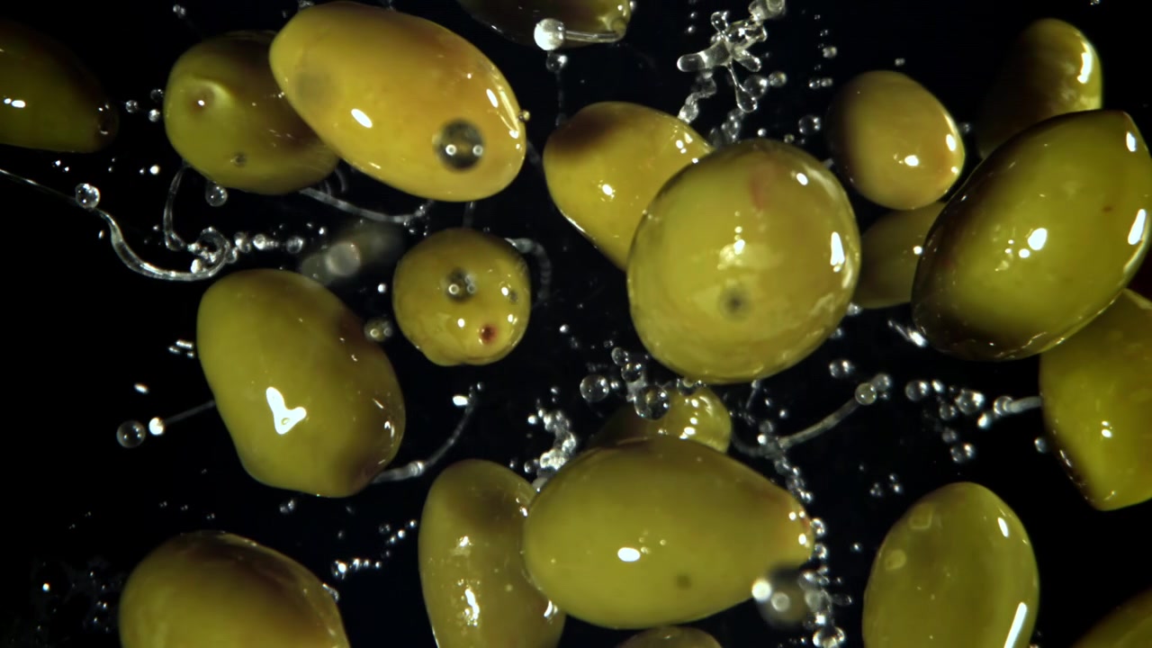Movimento rallentato di olive verdi che schizzano acqua su sfondo nero