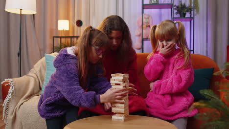 Three-siblings-children-girls-playing-with-blocks-board-game,-build-tower-from-wooden-bricks-at-home