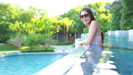 Happy-Satisfied-Asian-Woman-in-Swimsuit-and-Sunglasses-Enjoying-Her-Vacation-in-Pool-in-Tropical-Paradise