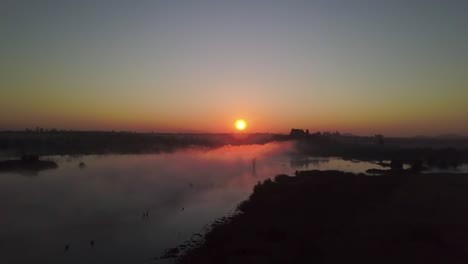 morning sun rises over the african bush creating beautiful colours in the sky and the low lying mist on the lake below.