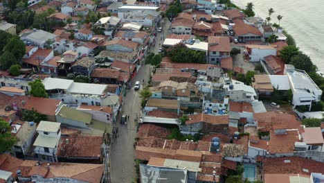 drone aéreo giratorio disparado mirando hacia abajo en la pequeña carretera de adoquines del centro de la famosa ciudad de playa tropical de pipa, brasil en río grande do norte con personas y coches que pasan por la carretera