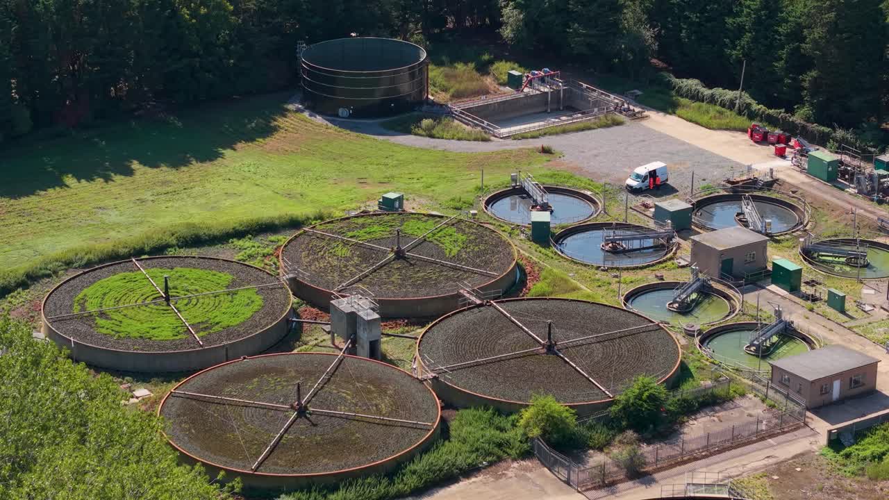 Aerial drone orbit of water treatment facility. Four large circular tanks dominate the scene with six smaller units behind them. Perfect for infrastructure, industry, and environmental projects