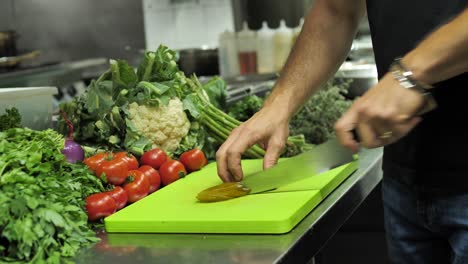 Chef-slicing-pickled-cucumber-on-cutting-board-in-restaurant-kitchen,-close-up