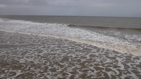 gentle waves from the ocean of the north sea rolling into the shore at the beach with white surf on a grey day on the english coast