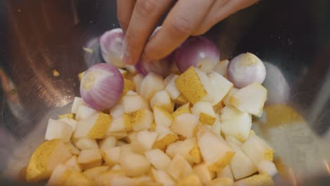 adding pear, onion and garlic ingredients into deep metal cooking bowl