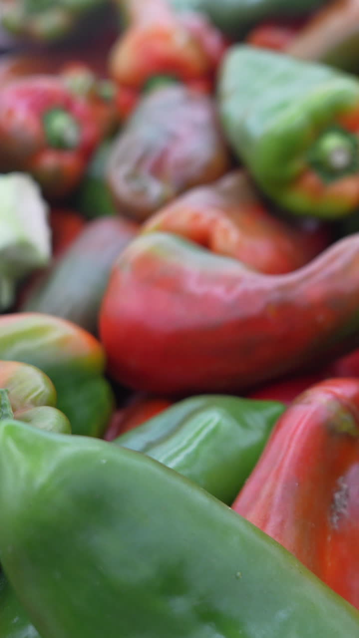 Vertical video capturing a close-up shot of vibrant green and red bell peppers, showcasing their glossy texture and vivid colors. Ideal for mobile and social media content