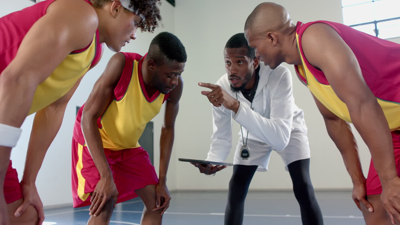Drei afroamerikanische Männer führen eine ernste Diskussion mit einem Basketballtrainer, der ein Tablet hält.