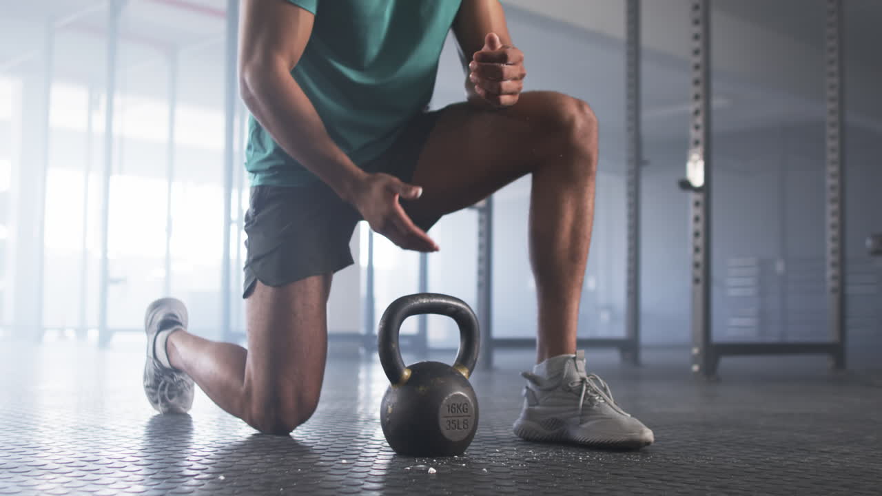 Kneeling in gym, man lifting kettlebell for strength training workout