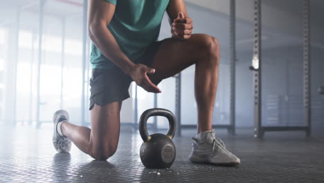 kneeling in gym, man lifting kettlebell for strength training workout